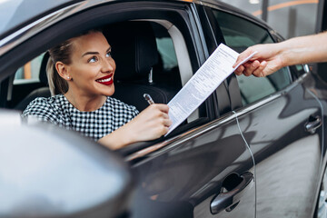 Obraz na płótnie Canvas Satisfied and smiled female buyer sitting in her new car. She happy while signing buyer's purchase contract with used car seller..