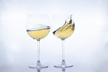 two white wine glasses with moving liquid on a greyish-white background