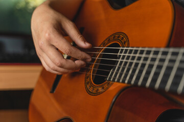 A young guy is playing a classical guitar in his room during the day