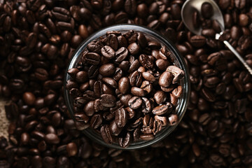 Lots of roasted coffee beans scattered on the table and in a glass jar. Focus on freshly roasted coffee beans in a jar, top view