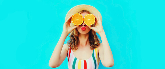 Summer portrait of cheerful young woman covering her eyes with slices of orange fruits and looking...