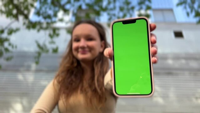 Teenage girl with loose hair brown hair brown hair dances with phone rejoices on the screen of lameness green screen beige background. High quality 4k footage