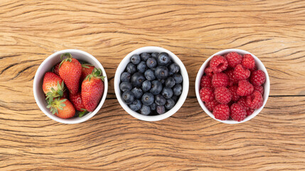 Raspberries, strawberries and blueberries in bowls over wooden table