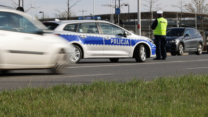 Policjant ruchu drogowego przy swoim radiowozie kontroluje ruch drogowy w mieście.  - obrazy, fototapety, plakaty