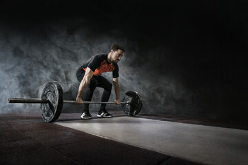 Fototapeta na wymiar Muscular men lifting deadlift in the gym with barbell. Dramatic interior gym with smoke. 