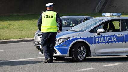 Policjant ruchu drogowego przy swoim radiowozie kontroluje ruch drogowy w mieście. 