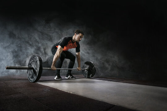 Muscular men lifting deadlift in the gym with barbell. Dramatic interior gym with smoke.	
