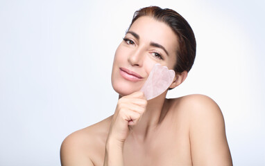 Beautiful woman with a quartz pink gua sha. Chinese traditional massage. skin care concept