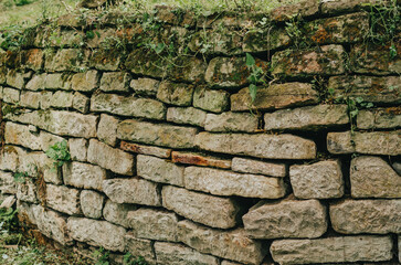 Paved wall with a rough, clear texture and deep lines between large stones. Laying an old fence. Destroyed stone fence.