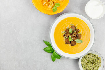 Seasonal autumn roasted pumpkin and carrot soup with cream and rye bread croutons on a light concrete background. Top view. Copy space.