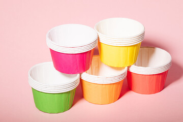 Multi-colored paper molds for muffins and cupcakes on a pink background