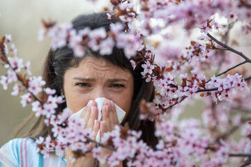 Girl wiping nose in front of blooming tree in spring