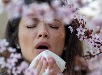 Girl sneezing in front of blooming tree in spring