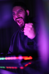 vertical photo A young man plays a computer game in a room with colorful neon lights. raising fists merrily with satisfaction in the black studio A man wearing headphones intends to play a game online