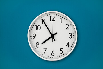 A white wall clock hangs on a blue wall with copy space and a central composition.