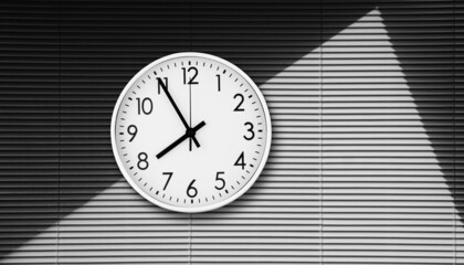 A large round clock hangs on a gray shuttered wall, modern design.