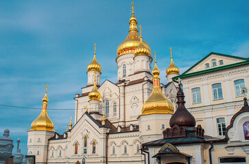 Fototapeta na wymiar The complex of the Orthodox monastery of the Pochaiv Lavra. Religious buildings. Side view of golden domes with crosses. Ukraine, 2022.