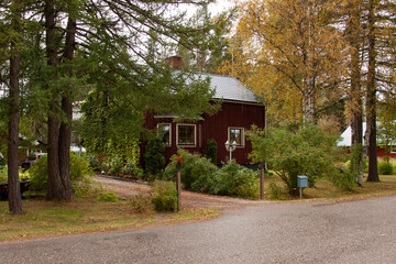 Red wooden house by the road surrounded by trees on an autumn day