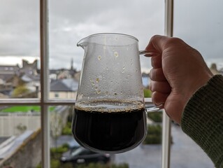 a hand holding freshly brewed filter coffee in a glass jar 