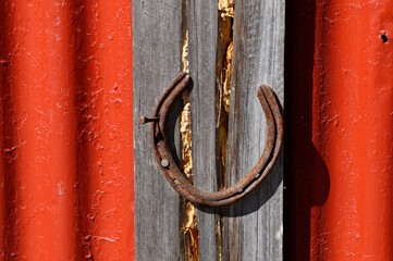 A rusty horse shoe is nailed to a rustic piece of wood on a red, corrugated iron building
