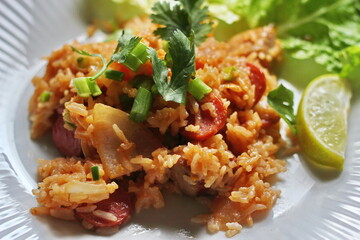 Pork and sausage fried rice served in a plate with lettuce and coriander garnish. Fried rice is a street food that is sold in Thailand.