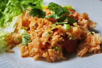 Pork and sausage fried rice served in a plate with lettuce and coriander garnish. Fried rice is a street food that is sold in Thailand.