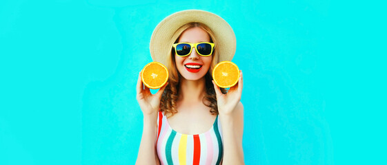 Summer portrait of happy smiling young woman with fresh slices of orange fruits wearing straw hat, sunglasses on blue background
