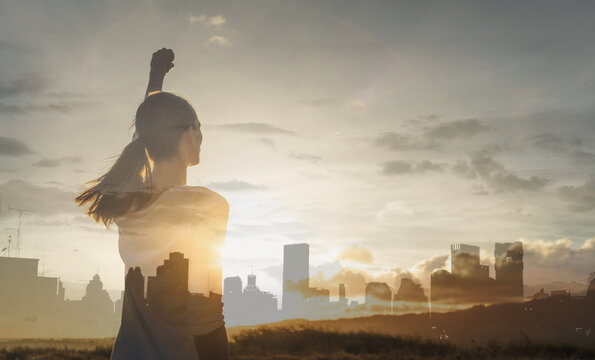 Modern day woman supper hero in the city. Strong young woman with fist In the sky facing the city sunset 