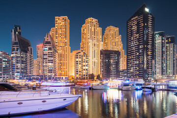 Fototapeta na wymiar Dubai Marina Port, UAE, United Arab Emirates - Jetty With Many Moored Yachts In Evening Night Illuminations. Night View Of Dubai Marina Towers.