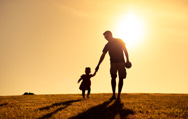 Silhouette of young father walking with his child holding hands  - obrazy, fototapety, plakaty