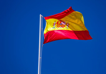 National flag of Spain on flagpole in clear sunny summer sky.