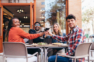 portrait of 4 smiling friends of different ethnicities toasting with red wine