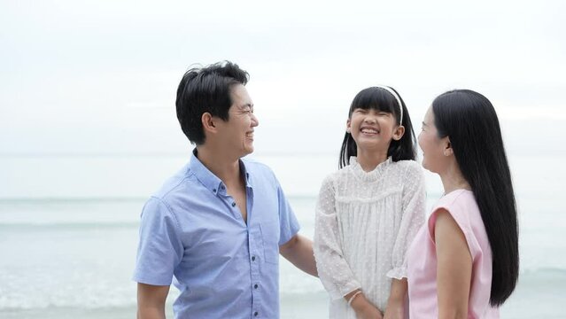Holiday concept of 4k Resolution. Daughter kisses mom and dad's cheeks on the beach. Young Asian girl smiling happily. parents-child relationship.