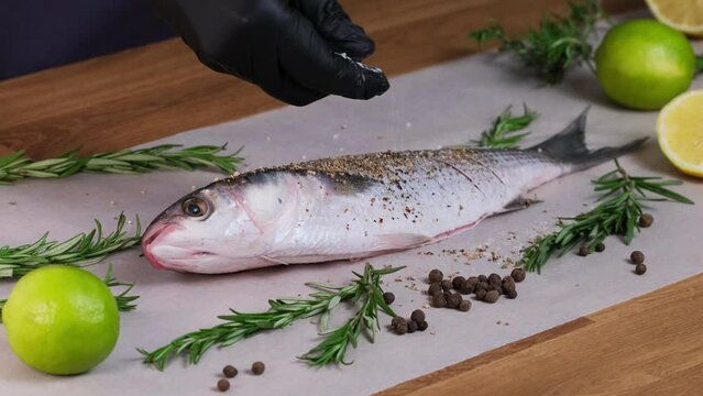 Mullet fish with marinade. Salt the dish with salt grinder. Spices and sauce are mixed with fish. Pepper the raw fresh fish for frying. Home kitchen, Culinary master class close-up slow motion