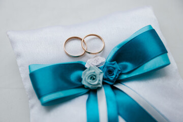 Two gold wedding rings lie on a festive pillow with a beryuz-colored bow, wedding details, wedding pillow, close-up