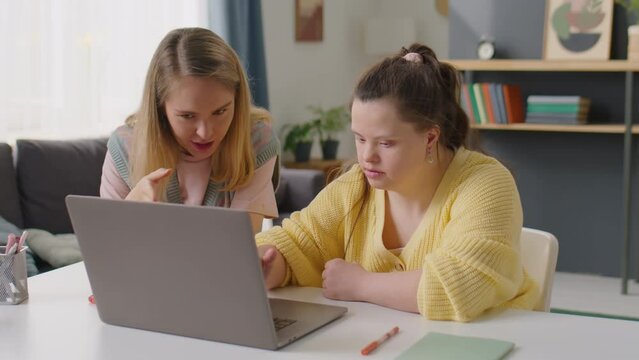 Girl with Down syndrome and female tutor using laptop and having discussion during home lesson