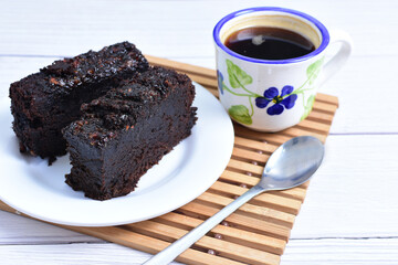 Traditional black ponque, with raisins, red wine flavor accompanied by a cup of coffee on a wooden background