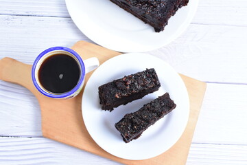 Traditional black ponque, with raisins, red wine flavor accompanied by a cup of coffee on a wooden background