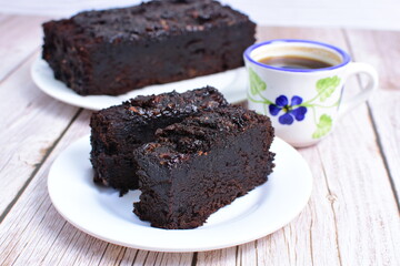 Traditional black ponque, with raisins, red wine flavor accompanied by a cup of coffee on a wooden background