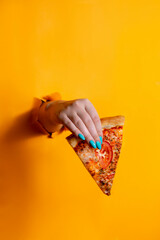 hands with manicure holding pizza slice against yellow background with copy space.