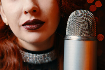 Close-up of women's lips painted with burgundy lipstick and retro microphone. Female singer with disco mic on bokeh light background. Redhead girl starting concert.