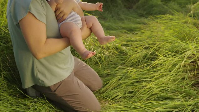 Mom teaches baby son walks on grass with bare feet. Baby daughter takes first steps with his mother on green grass in summer in park. Happy family playing in spring. Mom little feet baby close up