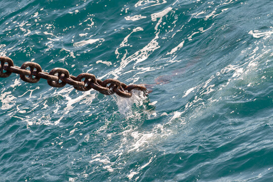 Anchor chain going dowm in the water with waves and splashes.