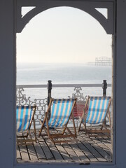 Classic deckchairs on a seaside pier with the wreck of another pier in the distance on a hot hazy day in Brighton