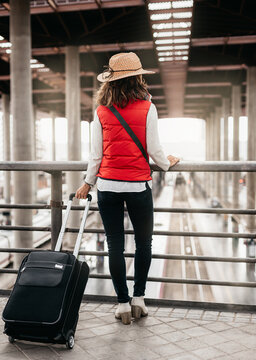 general view of a woman traveler with her back turned and leaning on a railing, observing the train station from above. travel and entertainment concept
