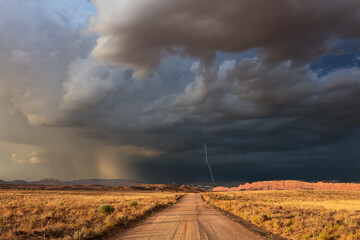 Dirt road with dark, ominous storm clouds and lightning - obrazy, fototapety, plakaty