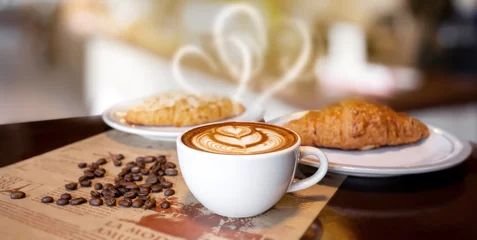 Crédence de cuisine en verre imprimé Café Hot latte coffee in white cup with heart shape smoke, with bakery and coffee beans placed on dark brown wood table, bakery and natural food, with light and dark,Italian and french cafe and croissant.