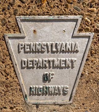 A Metal Sign In The Shape Of A Keystone With Pennsylvania Department Of Highways On It Shown On A Concrete Wall. The Plaque Signified Property Owned And Maintained By That Department