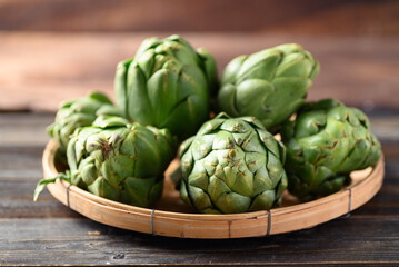 Obraz premium Green artichoke in bamboo basket on wooden background, Edible flower bud
