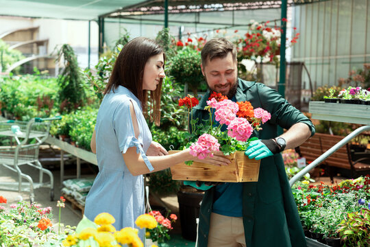 Worker helping female customer to buy flowers in garden center